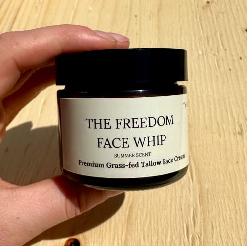 Customer holding a dark glass jar of The Freedom Face Whip against a wooden surface.