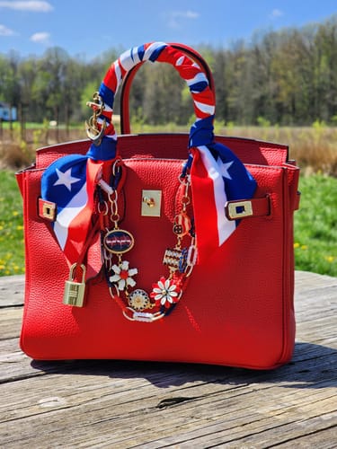 Customer's red LALUVA Warkin Bag decorated with a scarf and charms, sitting on a wooden surface outdoors.