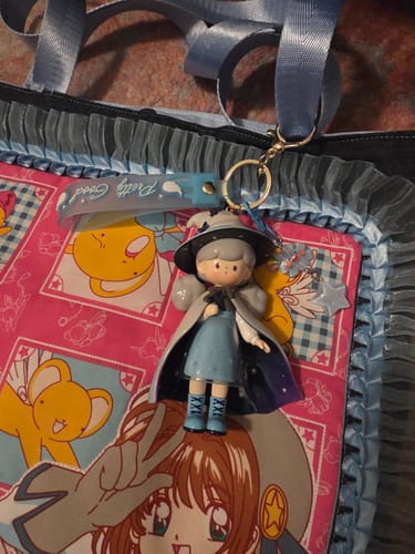 Customer's handmade keychain with a doll in a wizard hat and starry cloak hanging from a blue ruffled bag.