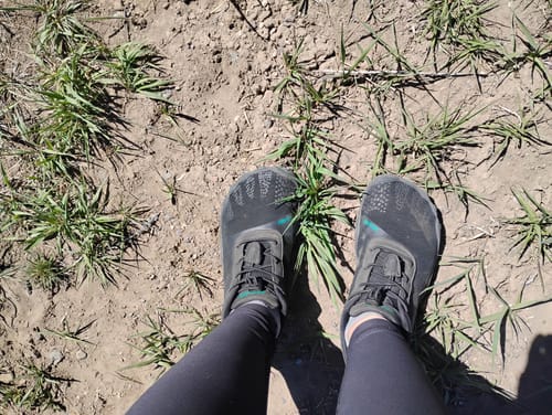 Reviewer wearing black Vitality III - Barefoot Shoes on a dirt path, seen from an overhead perspective.