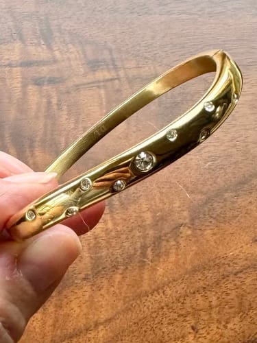 Close-up of a reviewer holding the gold Wave Bangle with Stones to show its details.