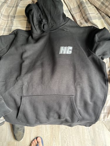 Client montrant son hoodie HC Argenté noir, posé à plat sur un lit.