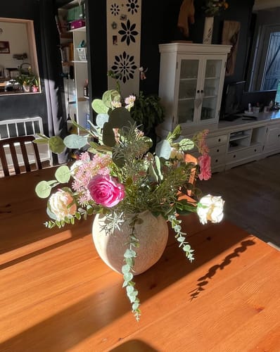 Recensents Boeket Flora staat in een lichte vaas op een houten tafel in de zon.