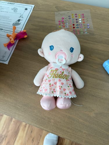 Customer's personalized baby girl doll, named 'Hailow', sitting on a table in a pink dress with a cherry and heart pattern.