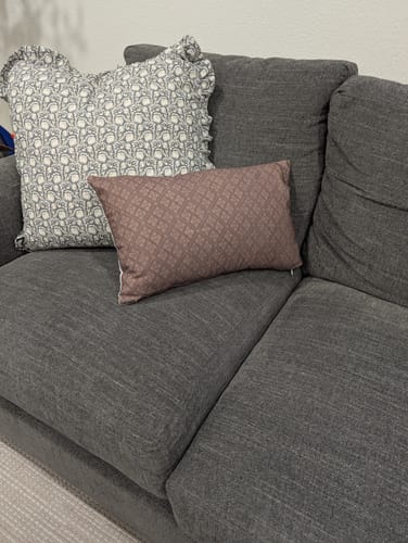 Customer's Quinn Ruffle pillow with its floral pattern, styled on a dark grey sectional with another pillow.