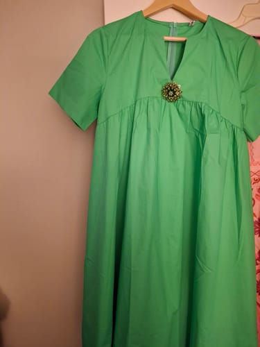 Customer's green short-sleeved dress with a decorative brooch at the neckline, hanging on a hanger.
