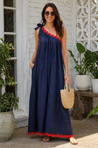 A reviewer smiles while wearing the navy blue A-line one-shoulder maxi dress, which features red scalloped trim and side pockets.
