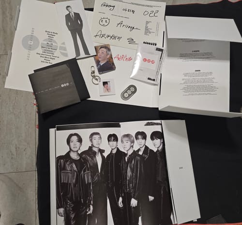 A reviewer's unboxed BTS - ARIRANG 5TH ALBUM, showing the poster, photocard, and other paper inclusions.