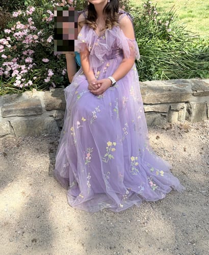 A reviewer sitting outdoors on a stone wall wearing the lavender Floral Embroidered Mesh Slit Dress.
