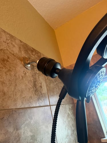 Reviewer's bronze Shower Head Filter installed in a tiled shower with a matching dark shower head.