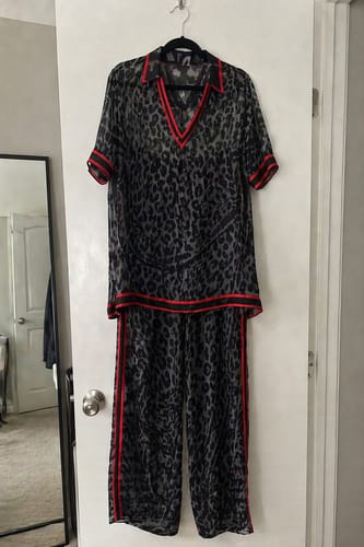 Customer's sheer leopard print pants and matching top with red trim hanging on a white door.