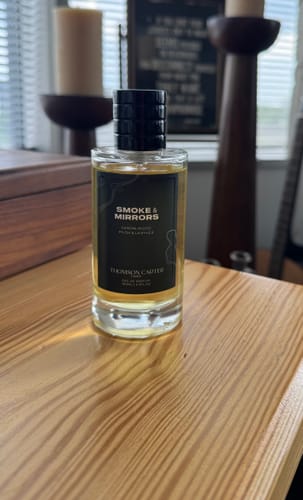 Reviewer's Smoke & Mirrors Eau de Parfum in a clear glass bottle on a wooden table.