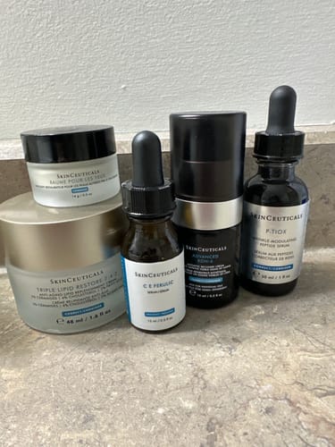 Reviewer's collection of SkinCeuticals products, including serums and creams, on a bathroom counter.