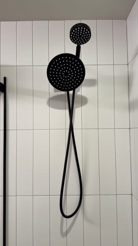 Customer's black dual shower head with a large rain head and smaller handheld head installed on a white tiled wall.