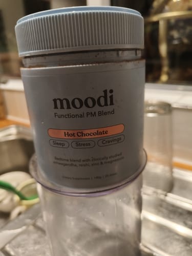 A reviewer's grey container of moodi PM Blend Hot Chocolate on a blender.