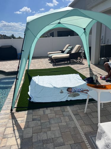 Customer's light blue Pop 'N Go Canopy set up by a pool, providing shade for a baby resting on a blanket underneath.