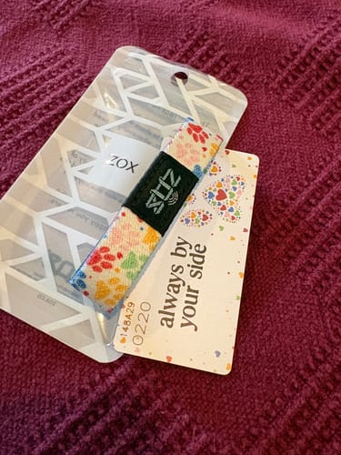 Customer's Dog Pack bracelet with colorful paw prints shown with its card reading 'always by your side'.