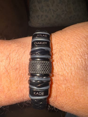 Customer wearing the personalized black bracelet on their wrist, featuring beads engraved with 'Atlas', 'Oakley', and 'Kade'.