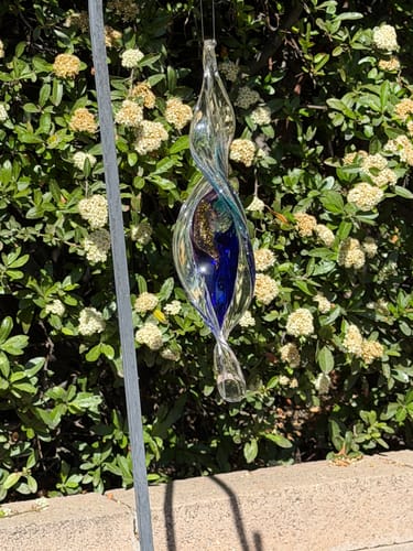 Customer's elegant Dichroic Spinner Suncatcher with blue and gold details hanging in a sunny garden.