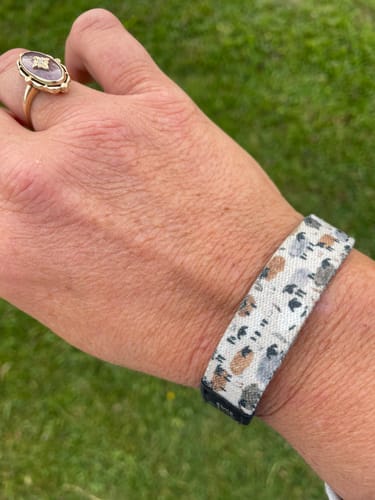 Customer's wrist wearing a light-colored Bible Verse Bracelet with a sheep pattern, shown outdoors.