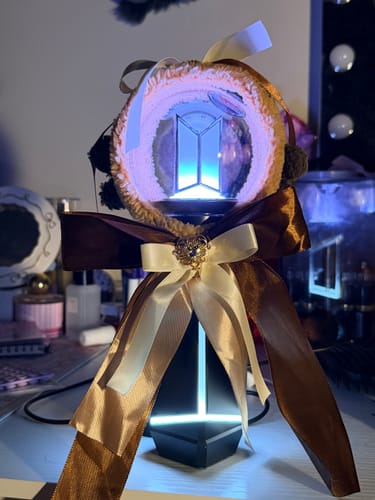 Customer's decorated BTS Official Light Stick Ver.4 Cradle, illuminated and holding the light stick on a desk.