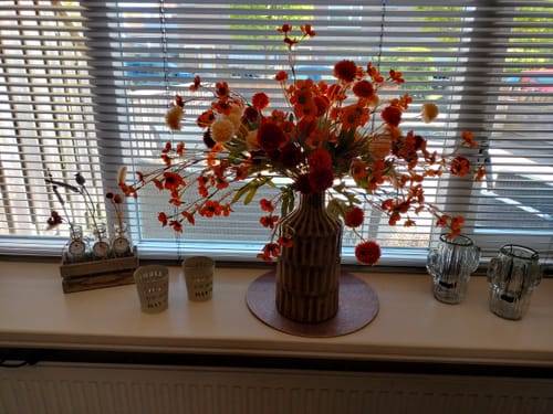 Recensent toont het warme oranje Wax Arrangement in een vaas op een vensterbank.