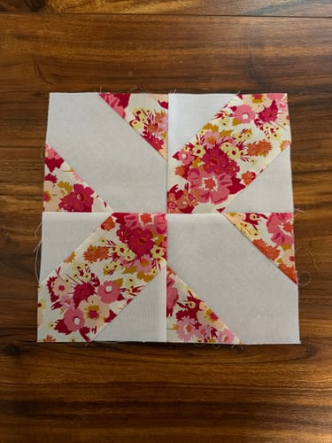 Reviewer's assembled quilt block from the Bloomcross kit, showing pink floral and solid white fabric in a cross pattern.