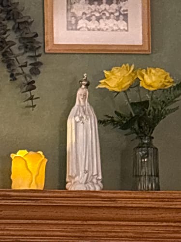 Reviewer's Our Lady of Fatima statue displayed on a wooden mantel next to a vase of yellow roses.