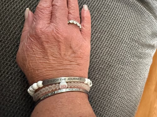 Reviewer's wrist showing the engraved 'ENJOY THE JOURNEY' bracelet stacked with other bracelets.