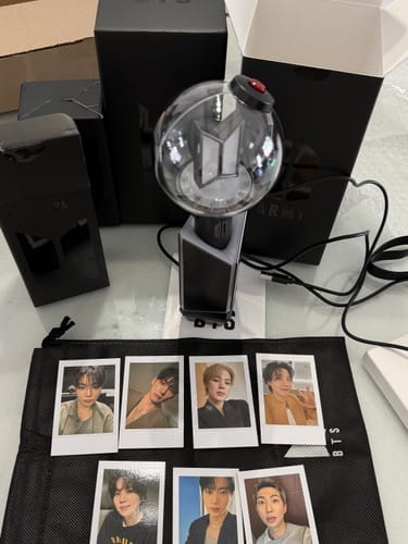 Reviewer's BTS Official Light Stick Ver.4 in its cradle, shown with packaging and seven member photocards on a pouch.