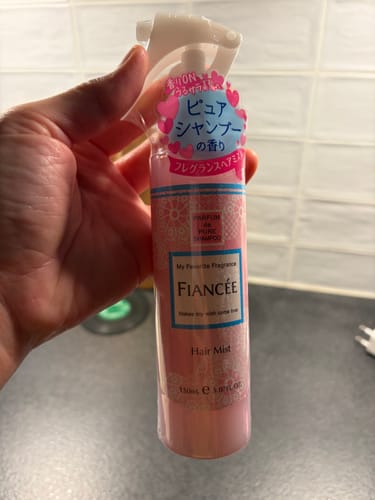 A customer holds up the pink bottle of Fiancee Hair Mist, showing its spray nozzle.