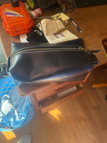 Reviewer's large blue leather toiletry bag with white contrast stitching, sitting on a desk.