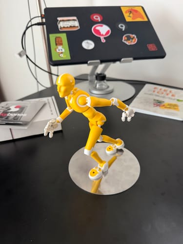 Customer's yellow LIGHT RAY Stickybones figure in a dynamic pose on its reflective metal pose plate on a desk.