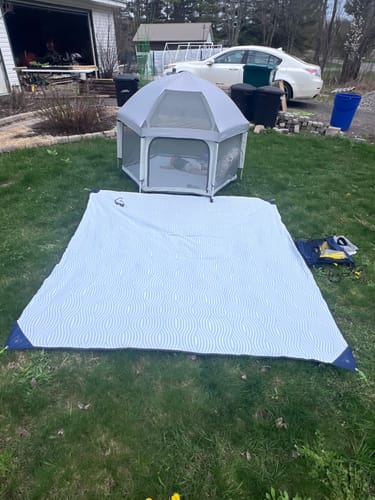 Customer's grey Pop 'N Go LUXE Playpen with a child inside, set up in a backyard with the matching mat laid out.