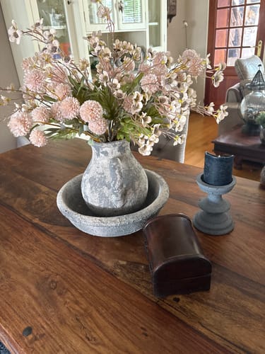 Het Wax Arrangement van een klant in een grijze, rustieke vaas op een houten eettafel.