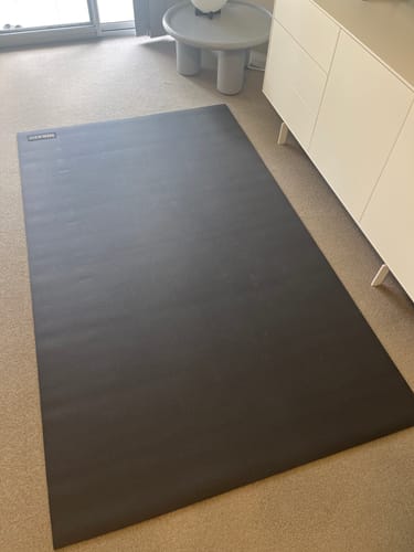 Customer's large, black Miramat exercise mat laid out on a carpeted floor in a room.