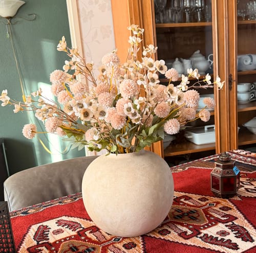 Recensent toont het Wax Arrangement - Crème in een grote, ronde, crèmekleurige vaas op een tafel.