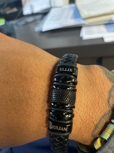 A close-up of a reviewer's wrist wearing the black personalized bracelet with the names 'Ellie' and 'Julian' engraved.
