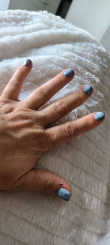 Hand einer Kundin mit aufgetragenen „Blue Silk“-Nagelfolien, die ein blaues Wellenmuster aufweisen.