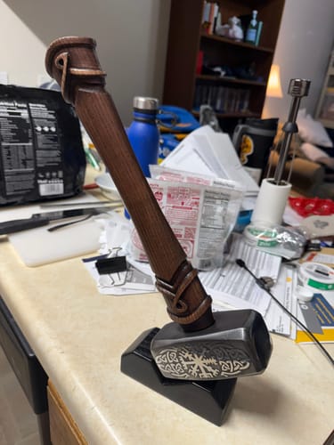 Customer's Handcrafted "Wayfinder" Hammer on a black stand, showing its engraved head and dark wood handle.