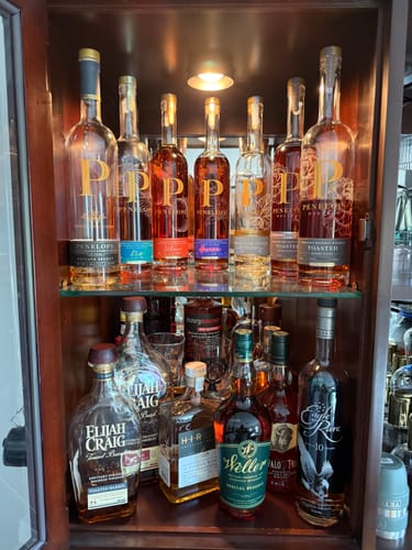 Customer's W.L. Weller and Buffalo Trace bourbon bottles displayed in a wooden liquor cabinet with their collection.