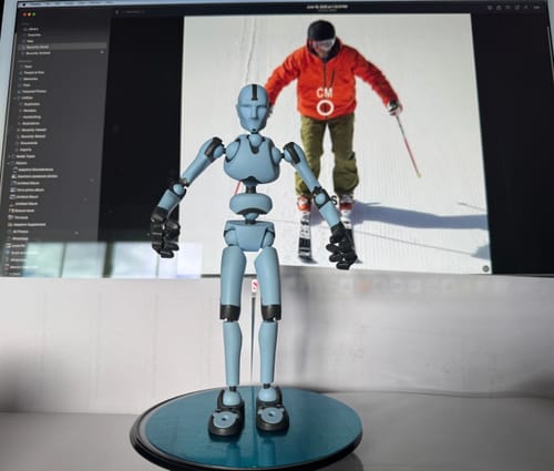 Customer's light blue Stickybones Figure on its stand, used to model a skiing position shown on a screen.