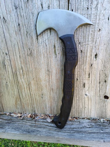 Customer's 'Navaro' tomahawk with its dark, engraved handle leaning against a weathered wood background.
