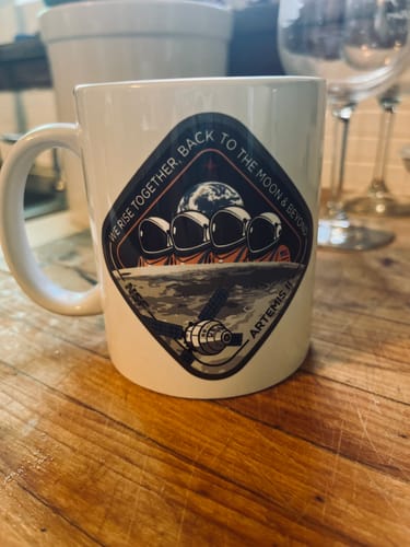 Customer's Artemis II Mug on a wooden counter, showing the detailed mission patch design.