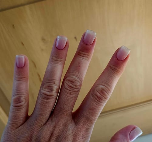 Hand einer Kundin, die die 'Babyboomer Pink' UV-Gel-Nagelfolien mit einem dezenten Ombré-Effekt nach fast zwei Wochen Tragezeit zeigt.
