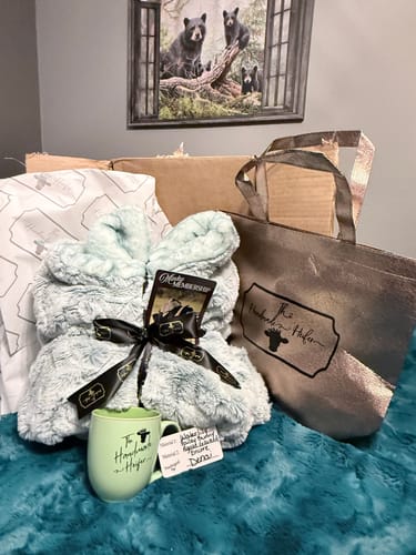 Customer's plush, light blue Travel Size Blanket displayed with a mug and tote from their subscription box.