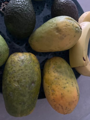 Kunde zeigt drei Papayas aus der Retterbox in verschiedenen Reifegraden neben anderem Obst.