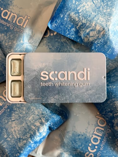 Reviewer's open metal tin of scandi gum with two pieces visible, resting on a bed of several product packets.