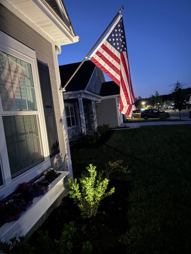 Reviewer's Prestige House Flag Pole kit with the American flag mounted on the side of their house at twilight.
