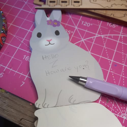 Customer's purple Eternal Inkless Pencil resting on a bunny-shaped notelet with handwriting.